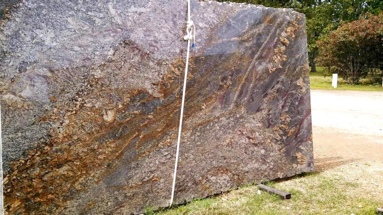 A large piece of granite is sitting on top of a lush green field.