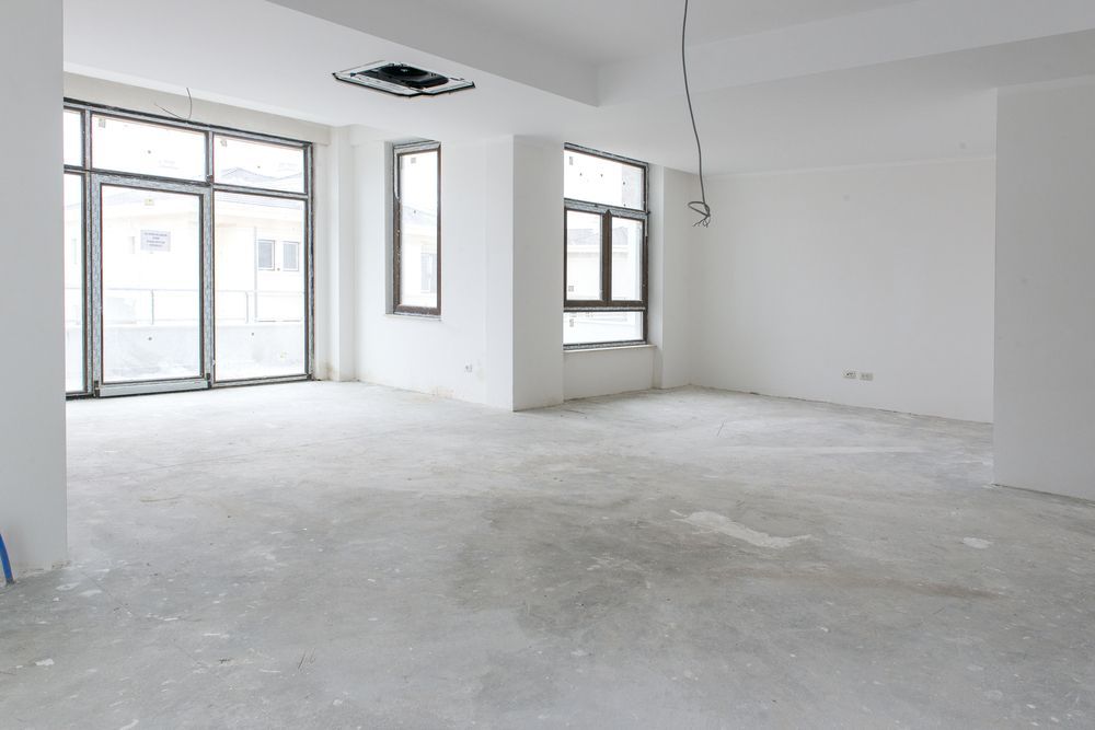 Empty unfinished white room with large windows and concrete floor