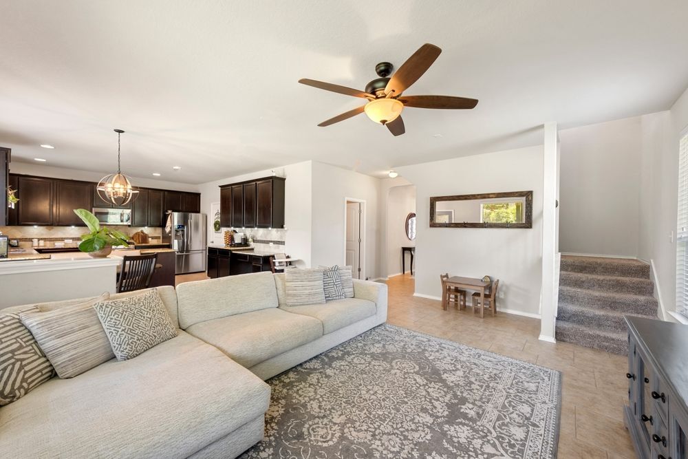Bright open-concept living room with sectional sofa, kitchen, staircase, and ceiling fan