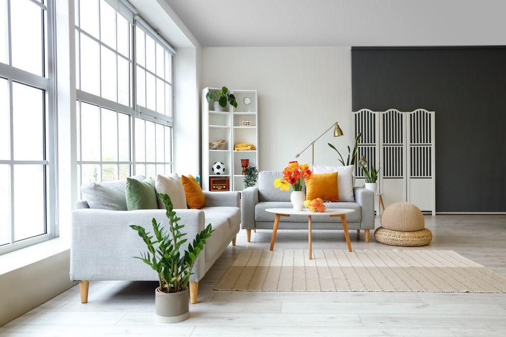 Bright modern living room with gray sofa, orange accents, large windows, and white shelves