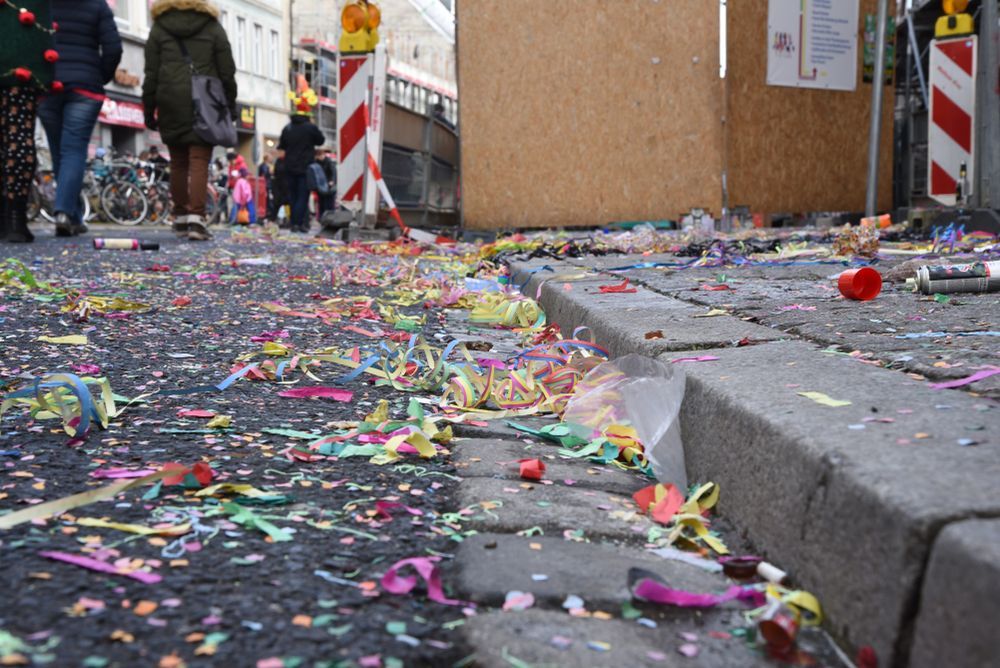 Confetti-covered street beside a curb after a celebration, with people in the distance.