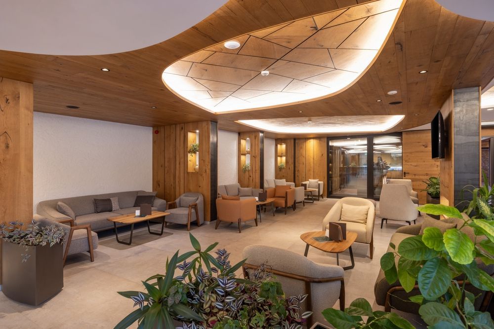 Modern hotel lobby with curved wood ceiling, warm lighting, sofas, chairs, and indoor plants