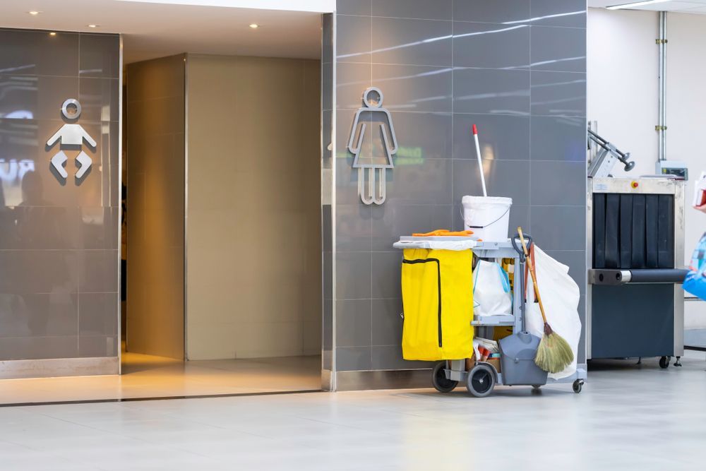 Hospital hallway with cleaning cart, mop bucket, and restroom-style figures on glass doors