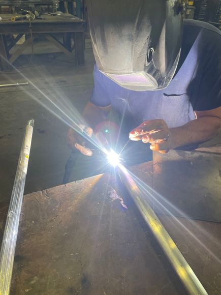 A man wearing a welding mask is welding a metal pipe.