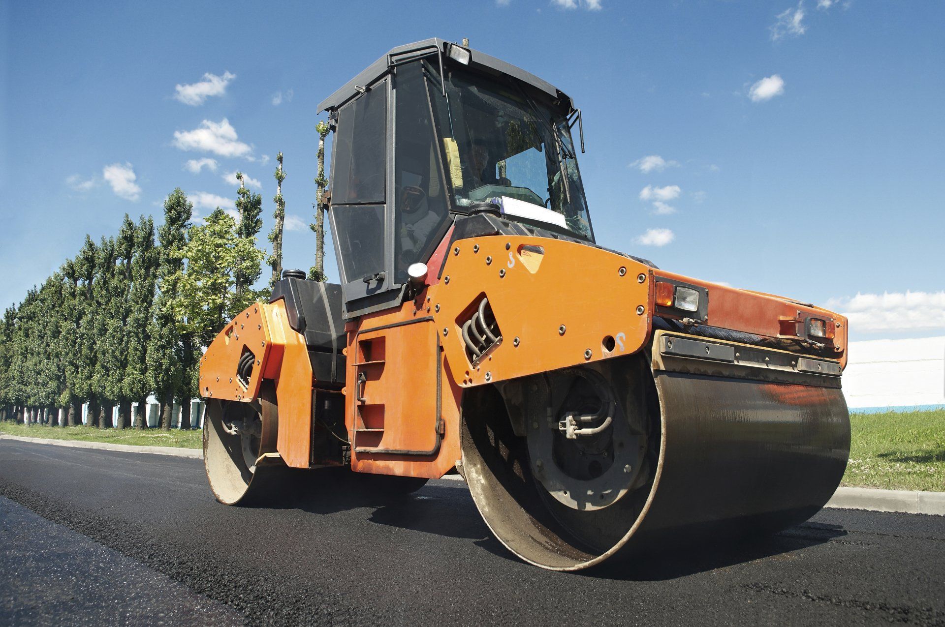 Orange road roller compacting asphalt on a road; blue sky background.