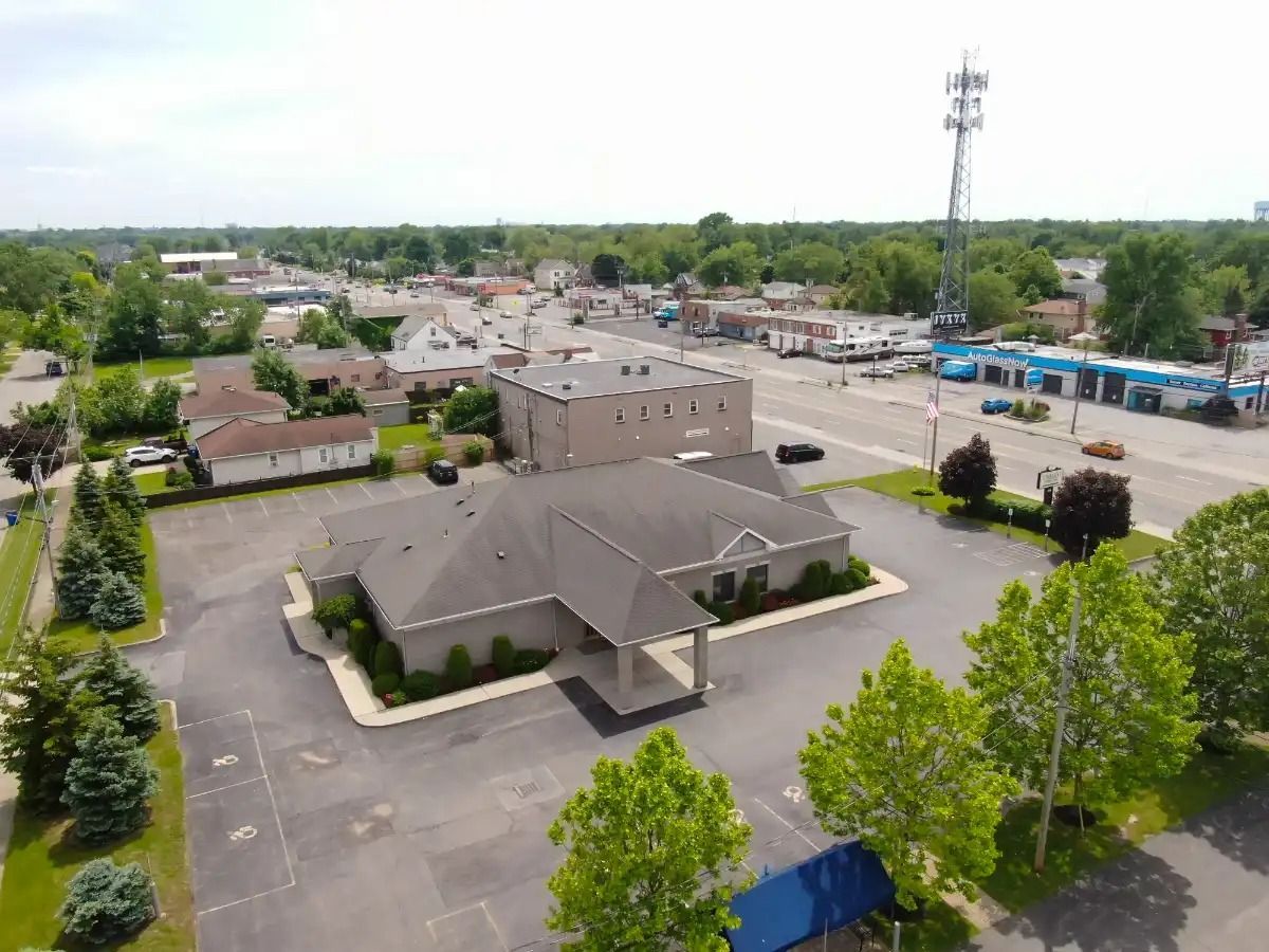 Aerial view of a building with a parking lot, set in a town with trees and a cell tower.