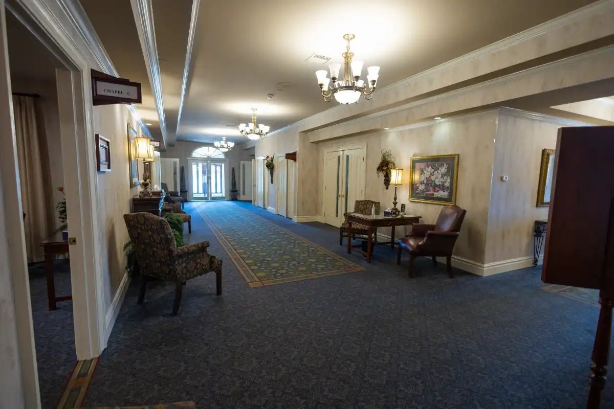 Long hotel hallway with blue carpet, ornate ceiling lights, and seating areas.