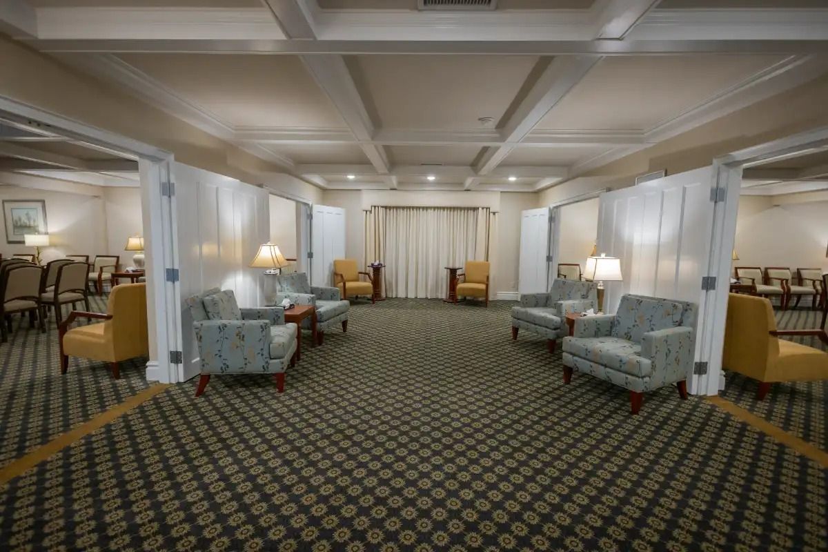 A room with patterned carpet, armchairs, and dividers. Yellow and blue chairs arranged for seating, soft lighting.