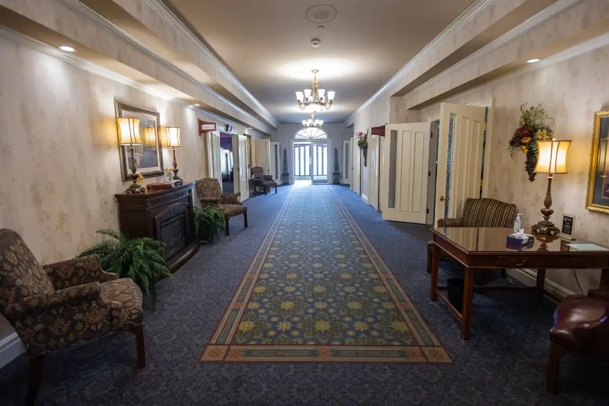 Long hallway with patterned carpet, chairs, and lamps. Doors line the walls.