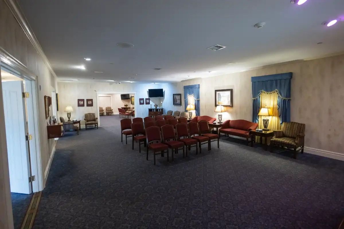 Funeral home chapel: rows of red chairs, blue carpet, tan walls, seating area with couches.