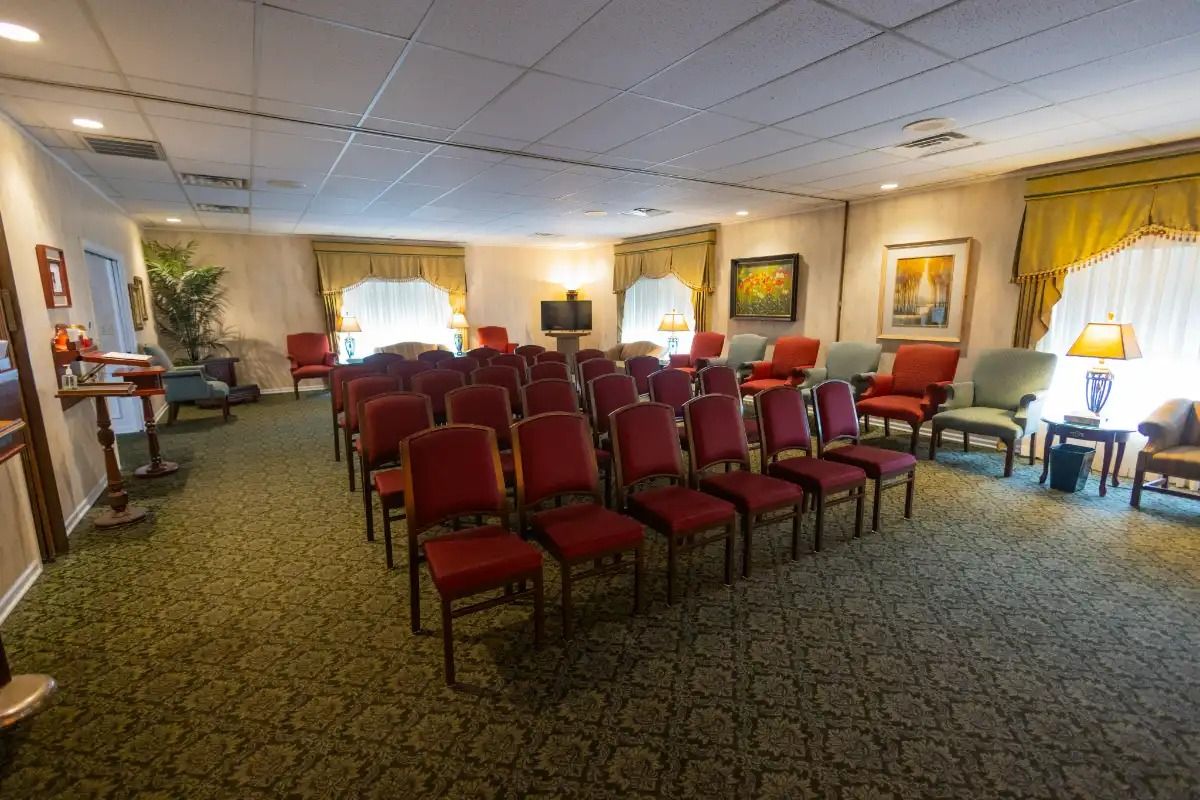Red chairs arranged in rows inside a room with green carpet and yellow curtains.