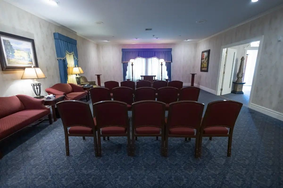 Funeral home chapel with red chairs, blue carpet, and window with blue curtains.