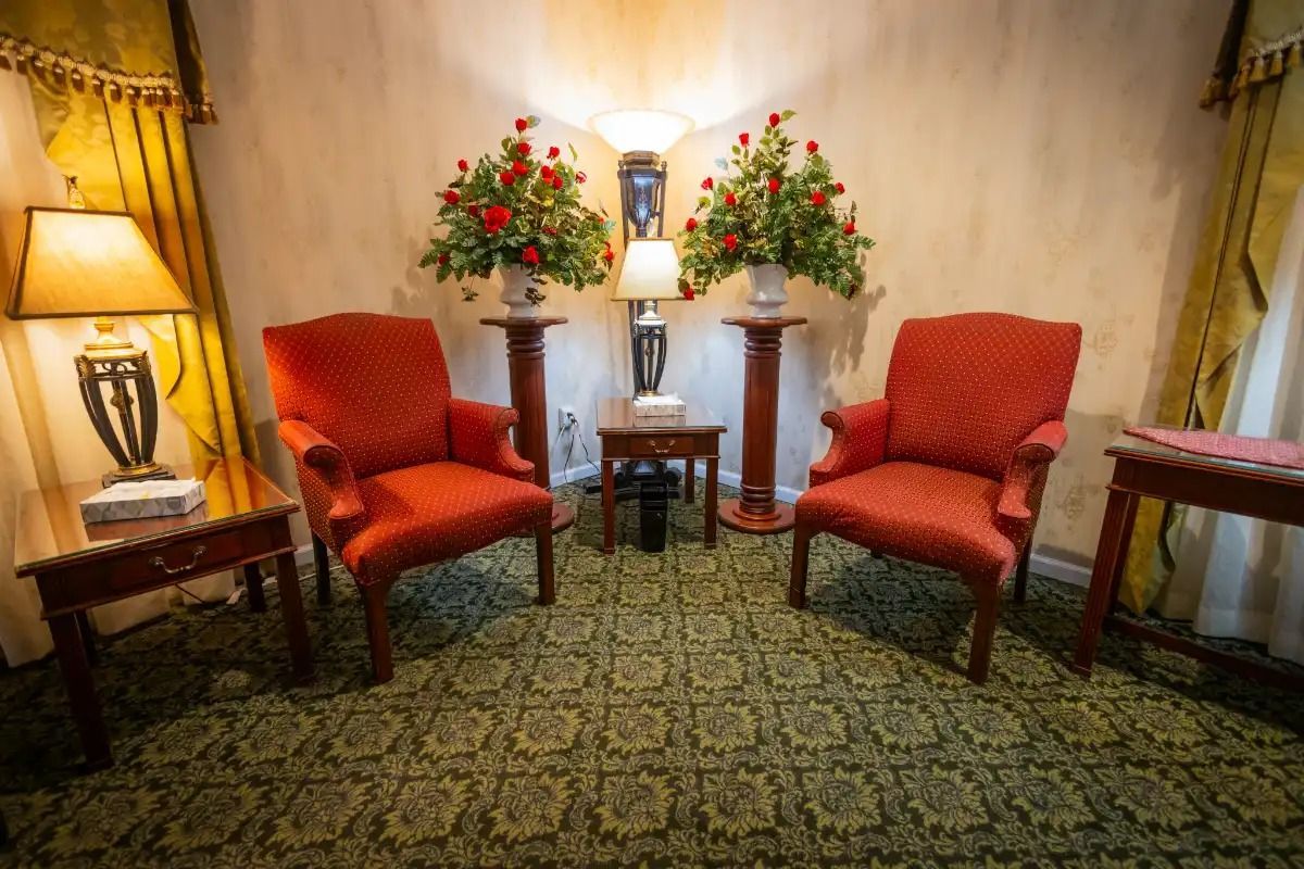 Two red armchairs face each other in a room, between two flower arrangements and a table.