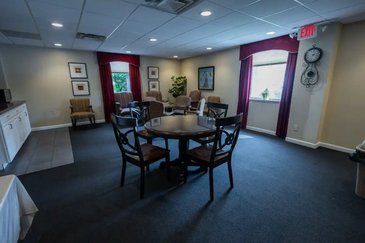A waiting room with a table and chairs. Red curtains, framed art, and cream walls.