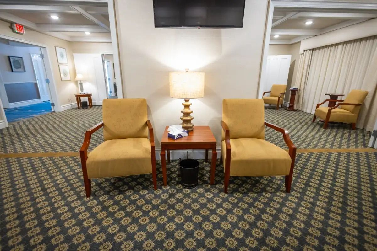Two yellow chairs face a small table with a lamp in a waiting room.
