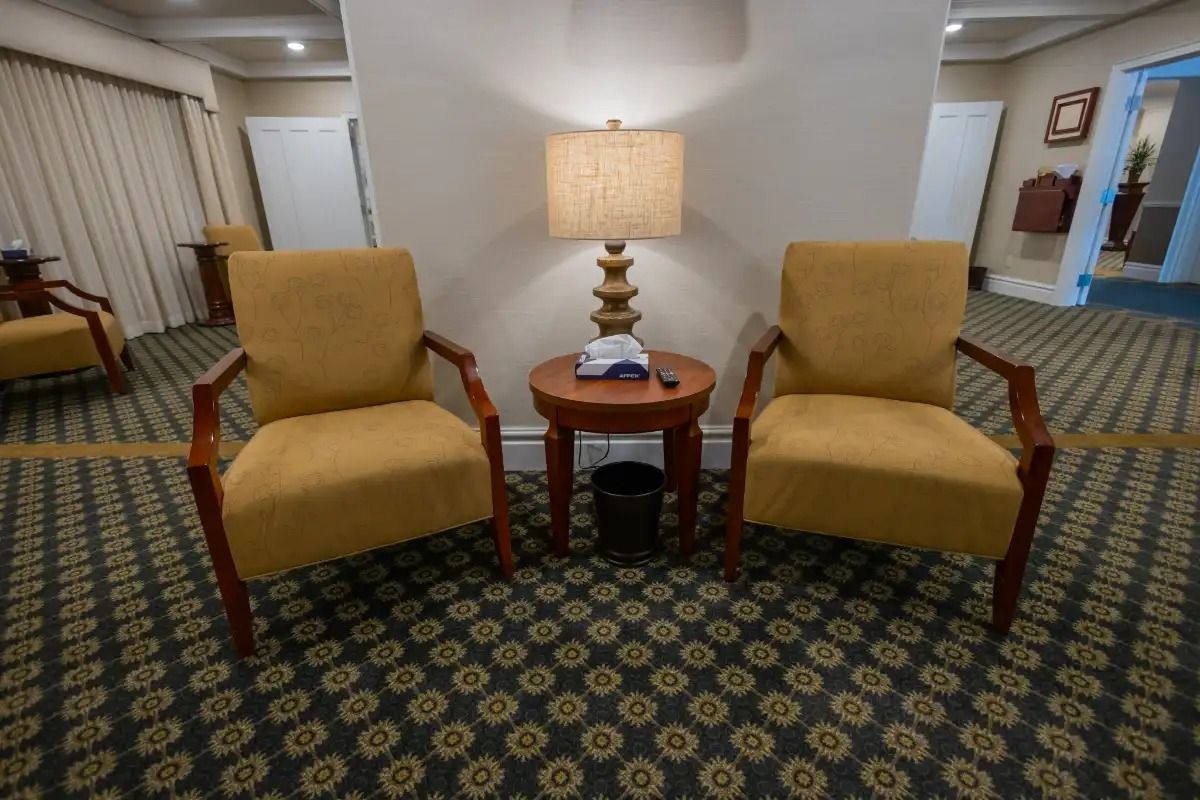 Two yellow armchairs face each other with a lamp table between them on a patterned carpet.