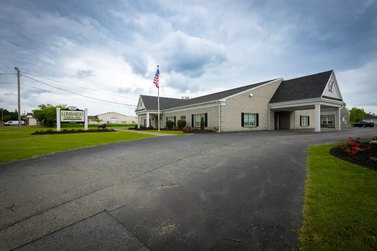 A light brick building with a long driveway and an American flag on a cloudy day.