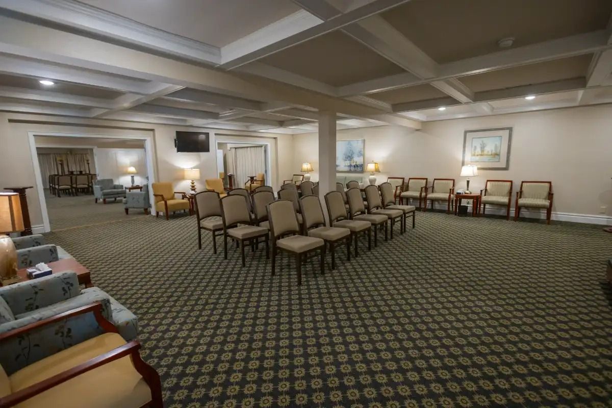 A funeral home viewing room with rows of chairs, neutral colors, and carpeting.