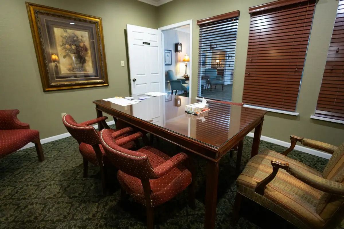 Office with dark wood desk, red chairs, and a framed painting. View into another room with a person.