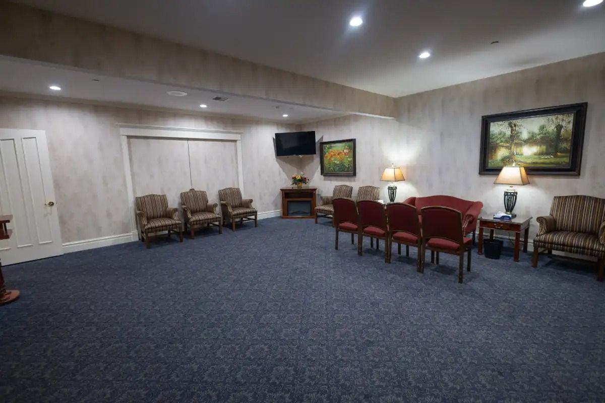 A viewing room with chairs, artwork, and a fireplace, in a neutral color scheme with blue carpet.