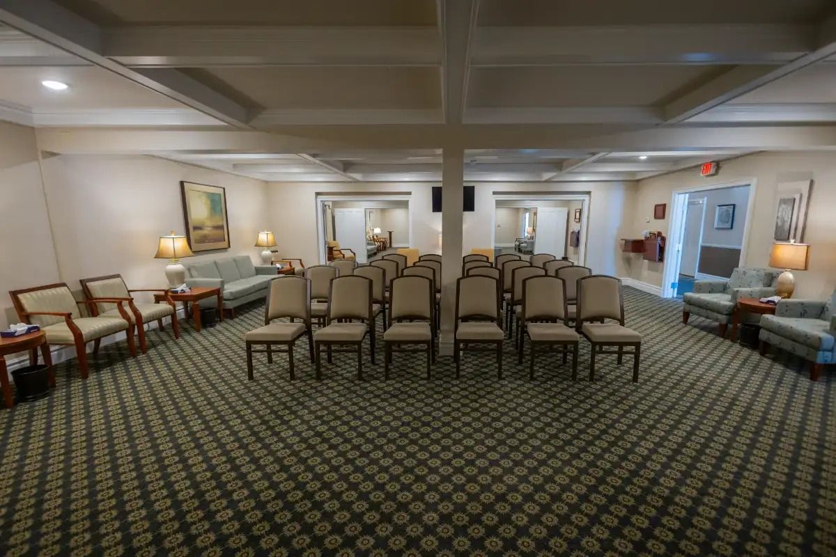 Rows of chairs face forward in a carpeted room. Sofas and armchairs flank the sides.