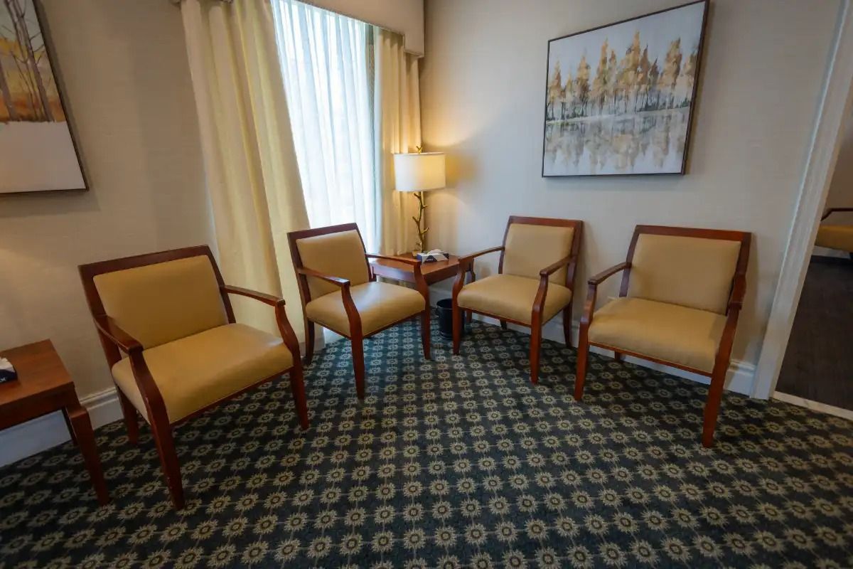 Four armchairs with yellow cushions in a room with patterned carpet and a painting.
