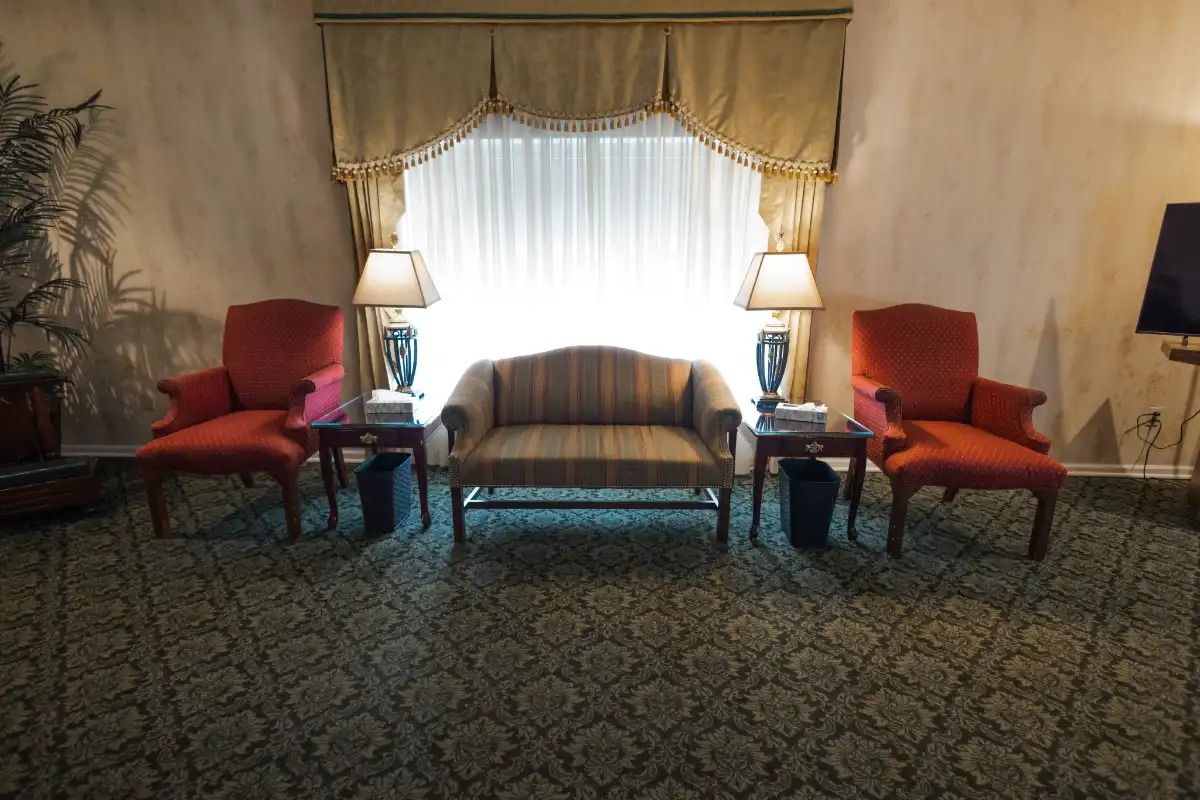 A room with two red chairs, a striped sofa, lamps, and a window with a decorative curtain.