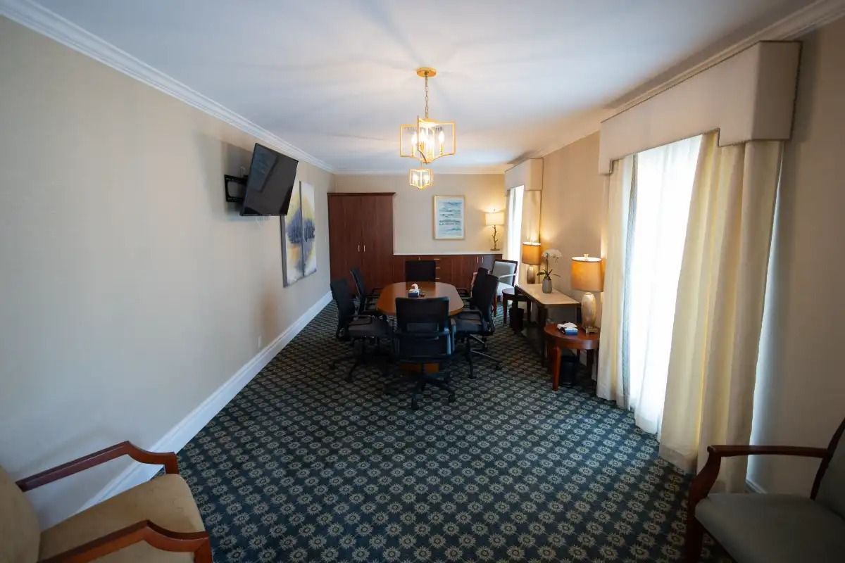 Meeting room with round table, chairs, and a TV on the wall; cream-colored walls, and patterned carpet.