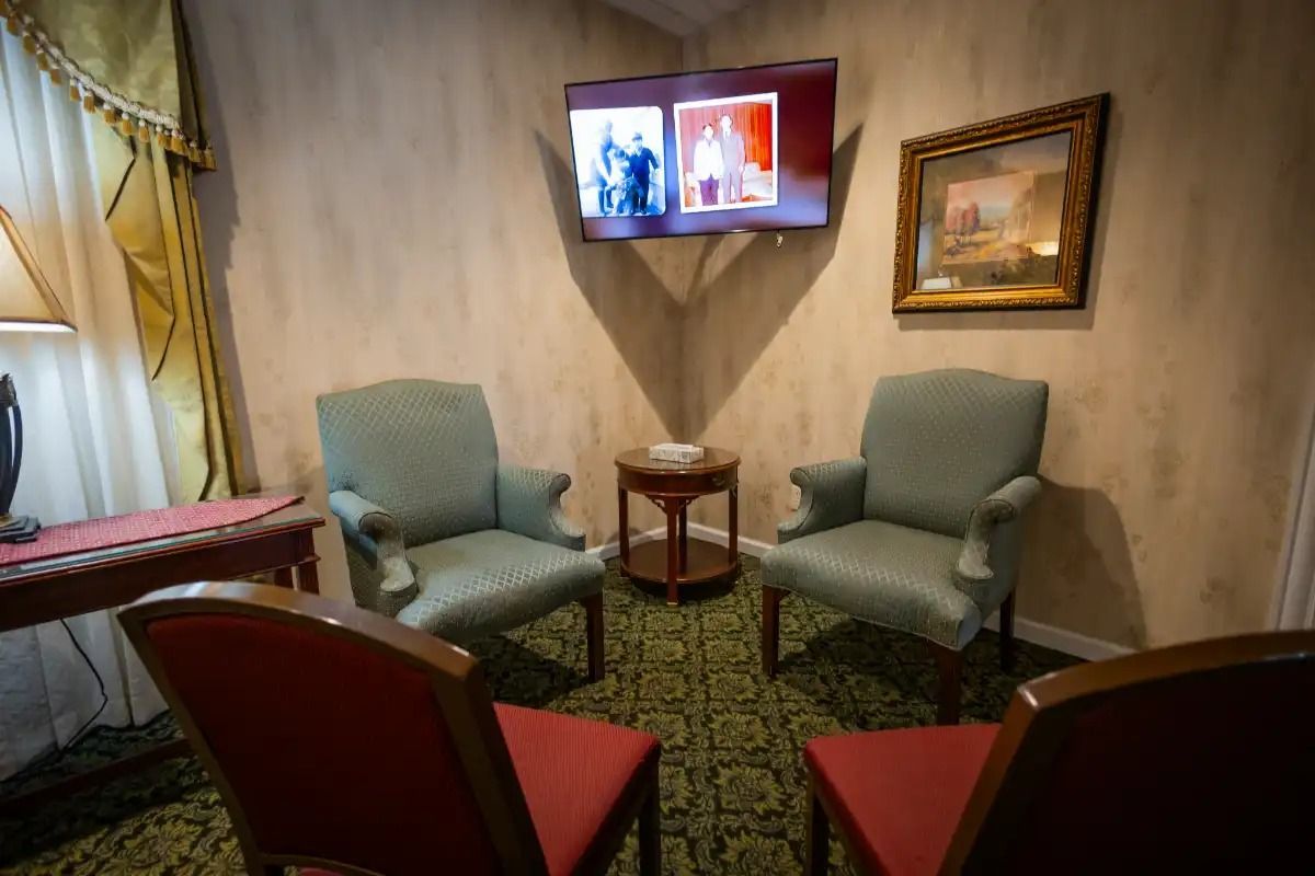A quiet room with armchairs and chairs surrounding a small table, a TV, and a framed painting.