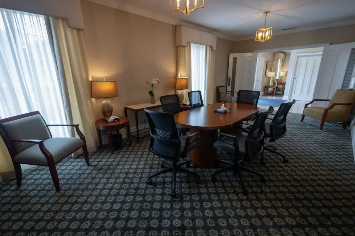 Meeting room with oval table, chairs, windows with curtains, and patterned carpet.