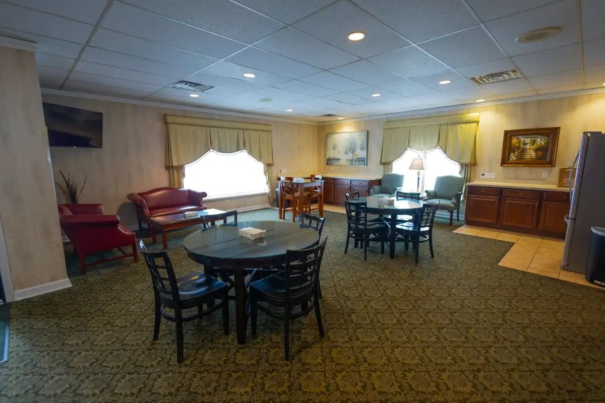 A waiting area with round tables, chairs, a red sofa, and cabinets; light green carpet.