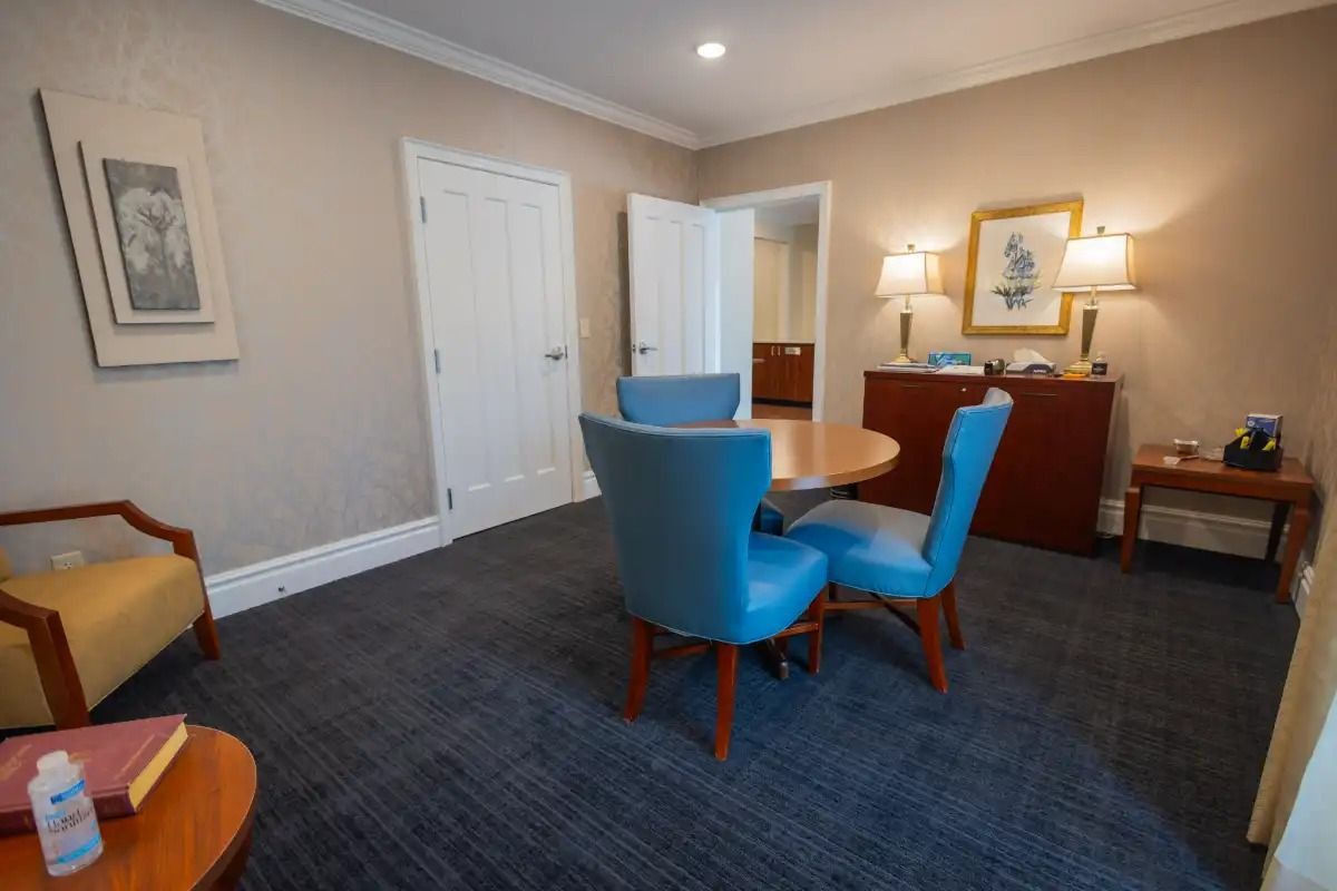 A room with a round table and blue chairs, a side table, and artwork.