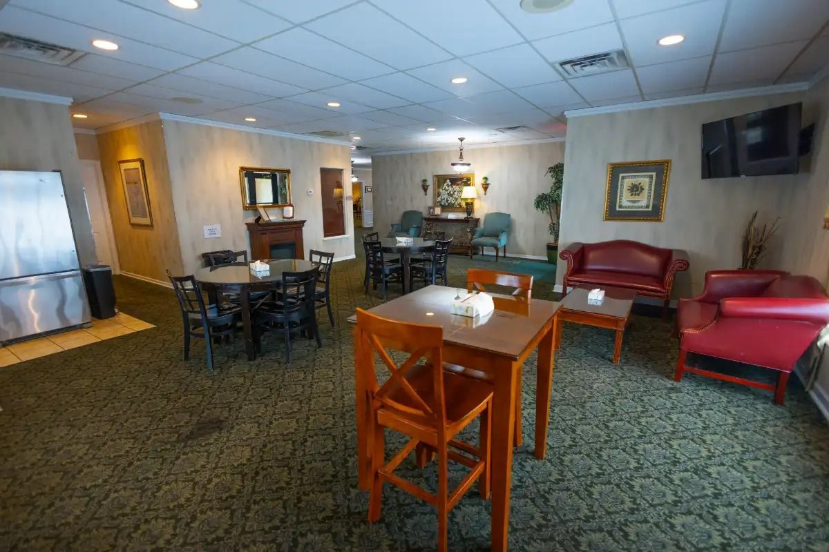 Lounge area with tables, chairs, and couches; carpeted floor, decorative walls, and appliances.