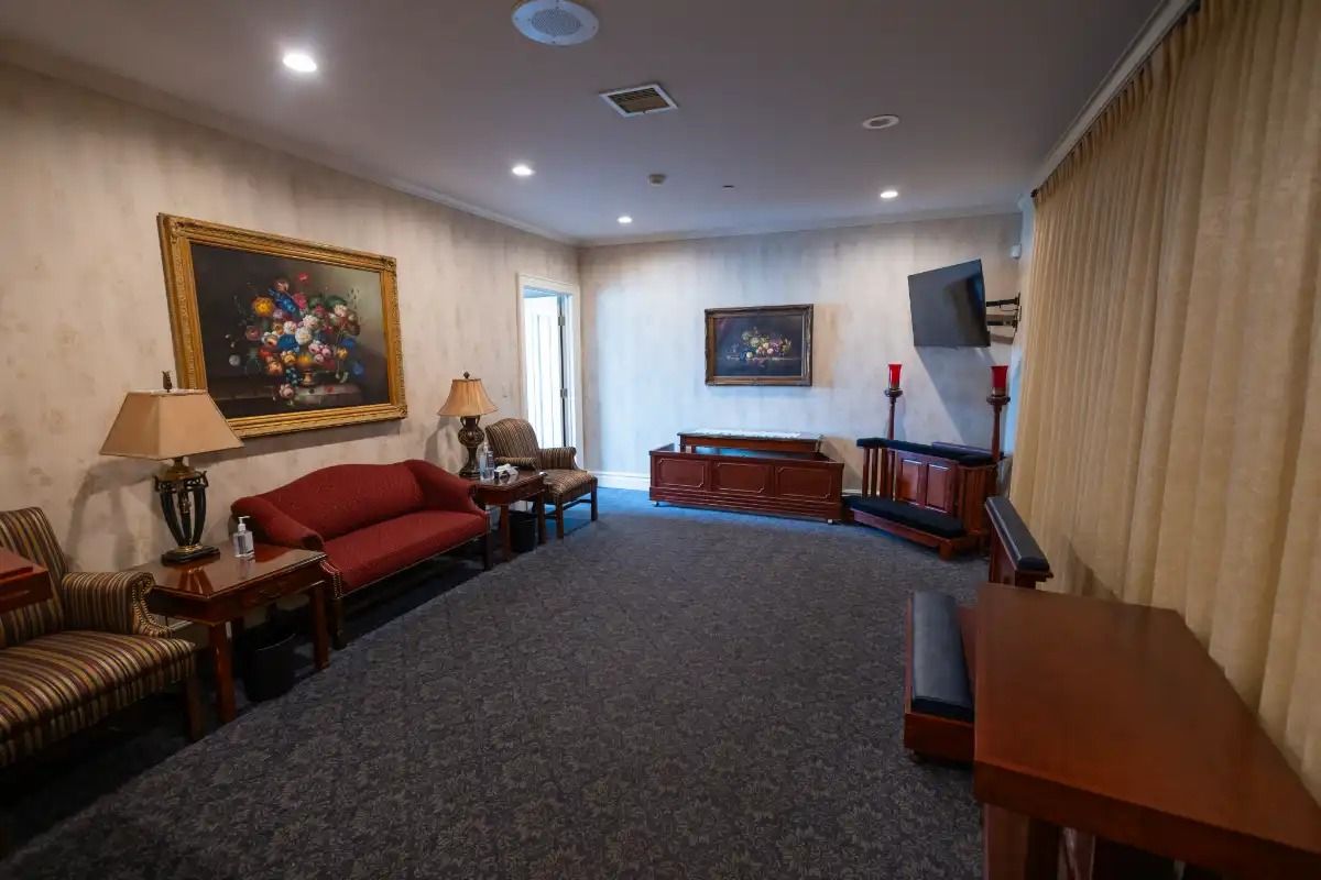 Interior of a funeral home waiting area with seating, paintings, and a TV.