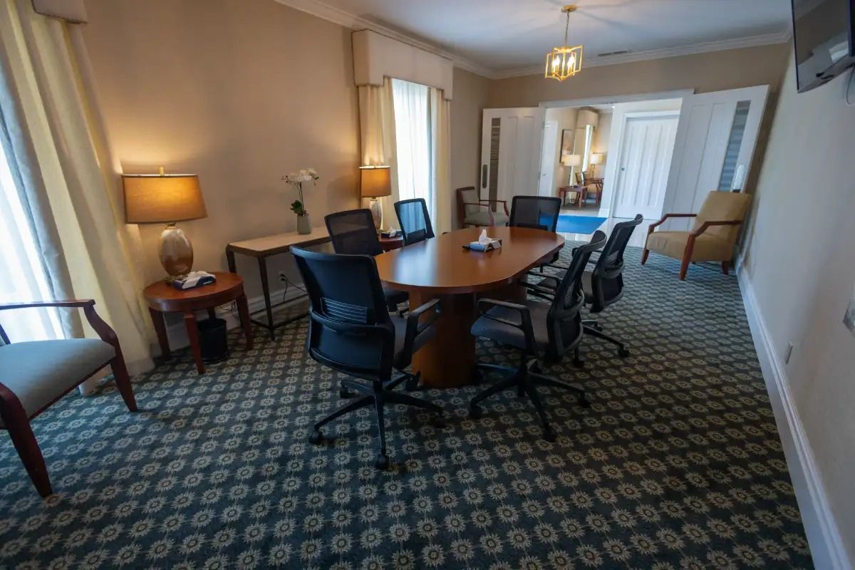 Meeting room with oval table and black chairs, beige walls, carpet, and window.
