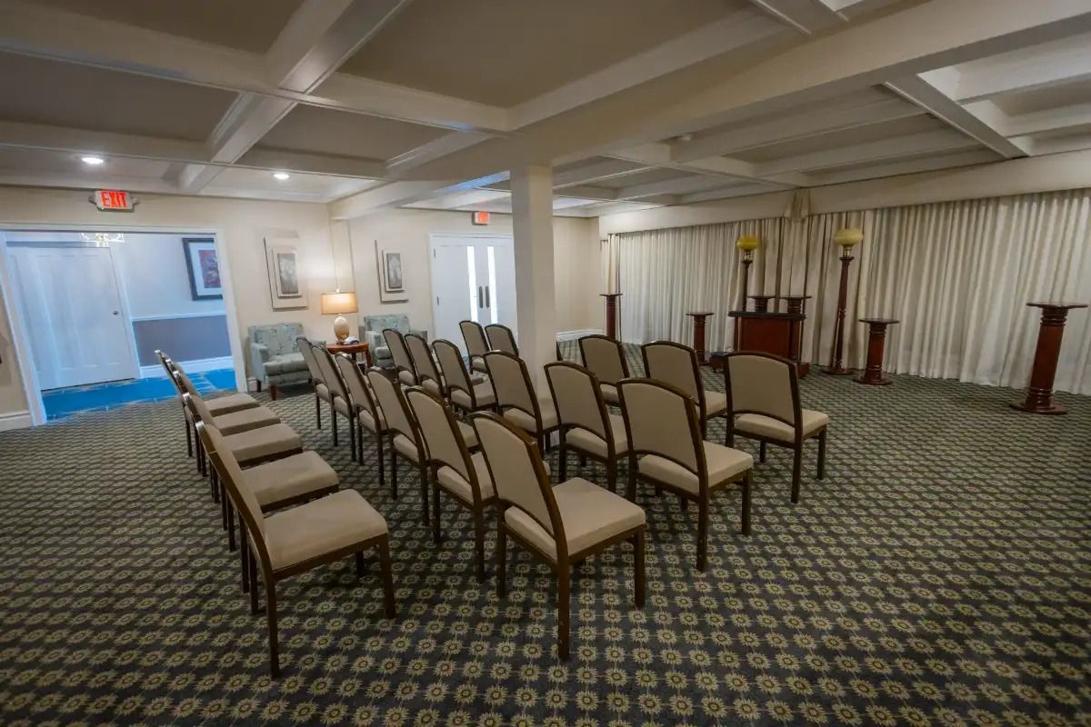 Rows of beige chairs face a small altar in a carpeted, windowed room.