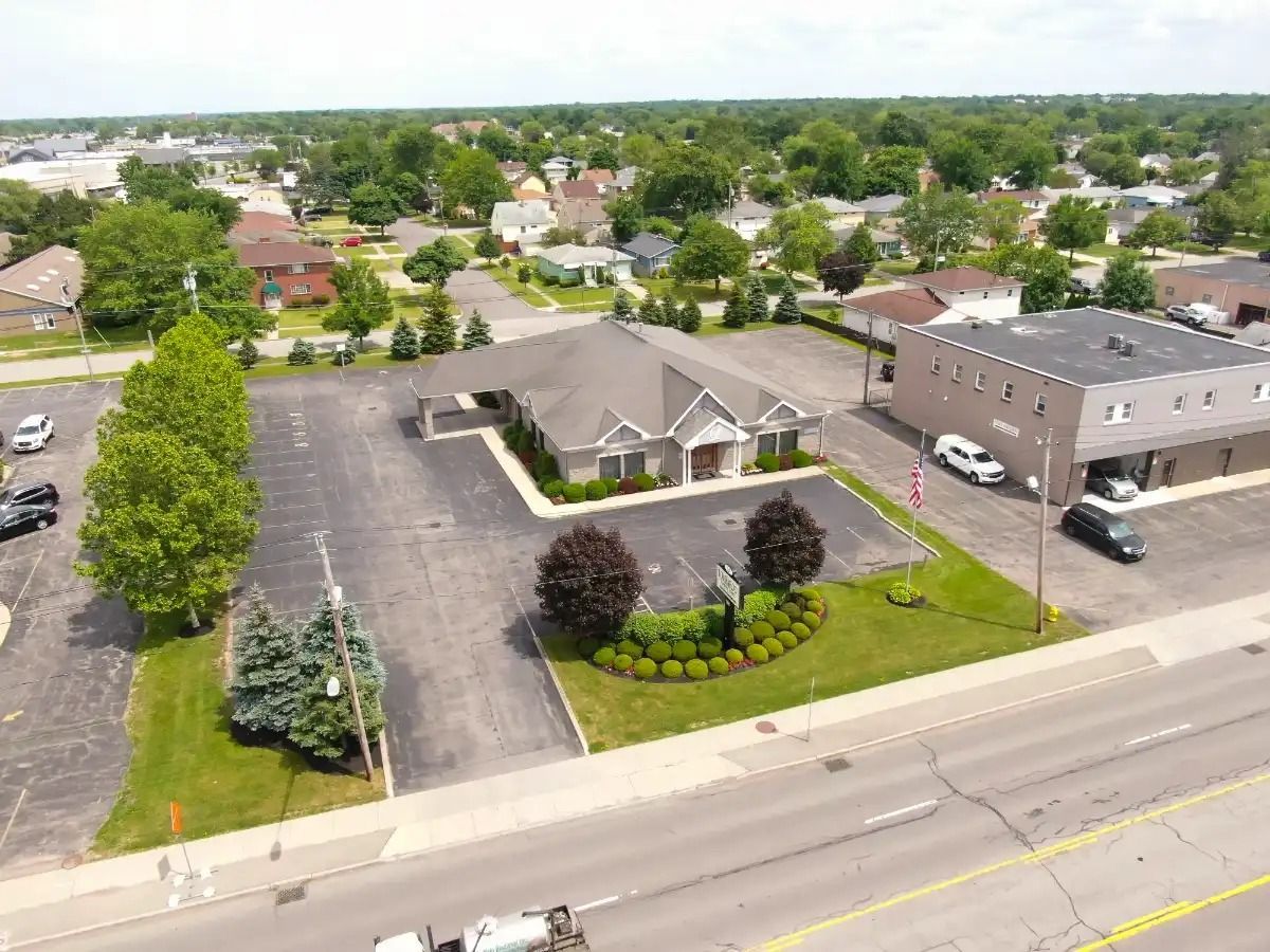 Aerial view of a commercial building with parking, surrounded by trees and residential area.