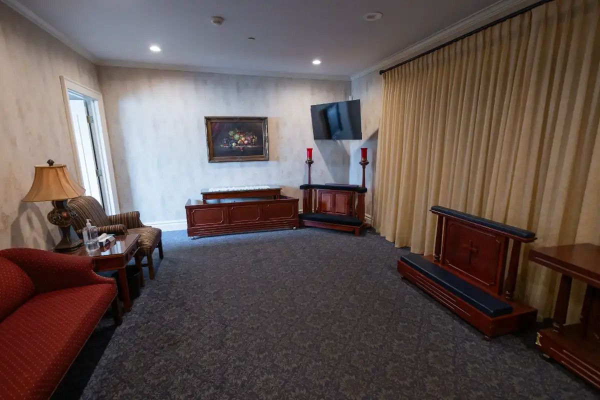 Funeral home interior: red sofa, wood furnishings, dark carpet, artwork, and a TV.