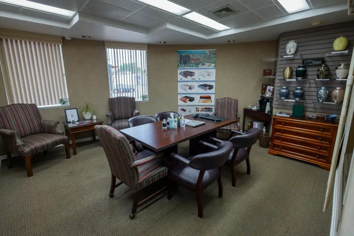 A meeting room with a table and chairs, urn display, and two windows.