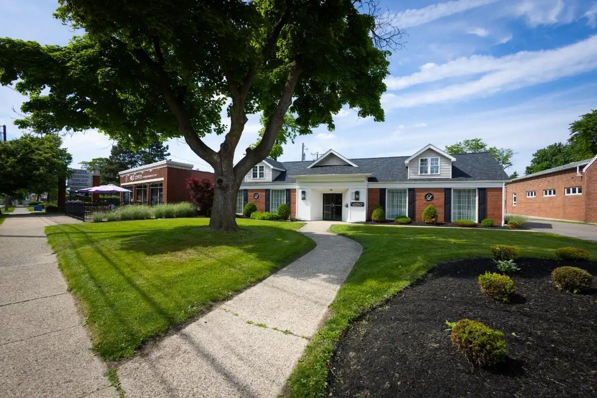 A building with a walkway, a large tree, and green grass under a bright blue sky.