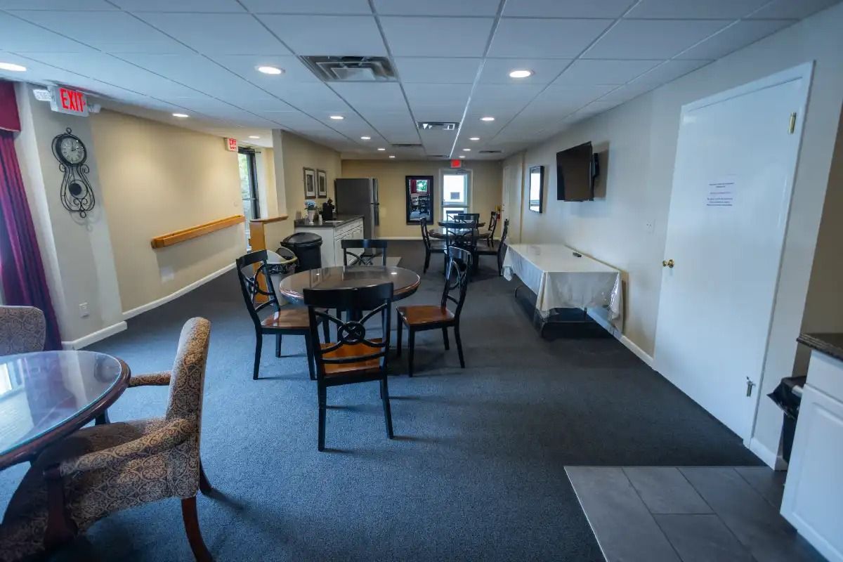 A long room with tables and chairs for a gathering. A hallway extends to the back.