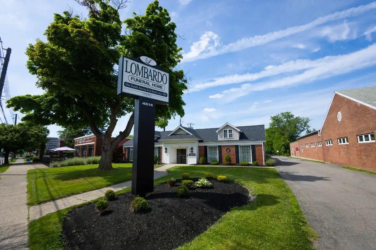 Sign for Lombardi Funeral Home in front of a white building, with a blue sky overhead.