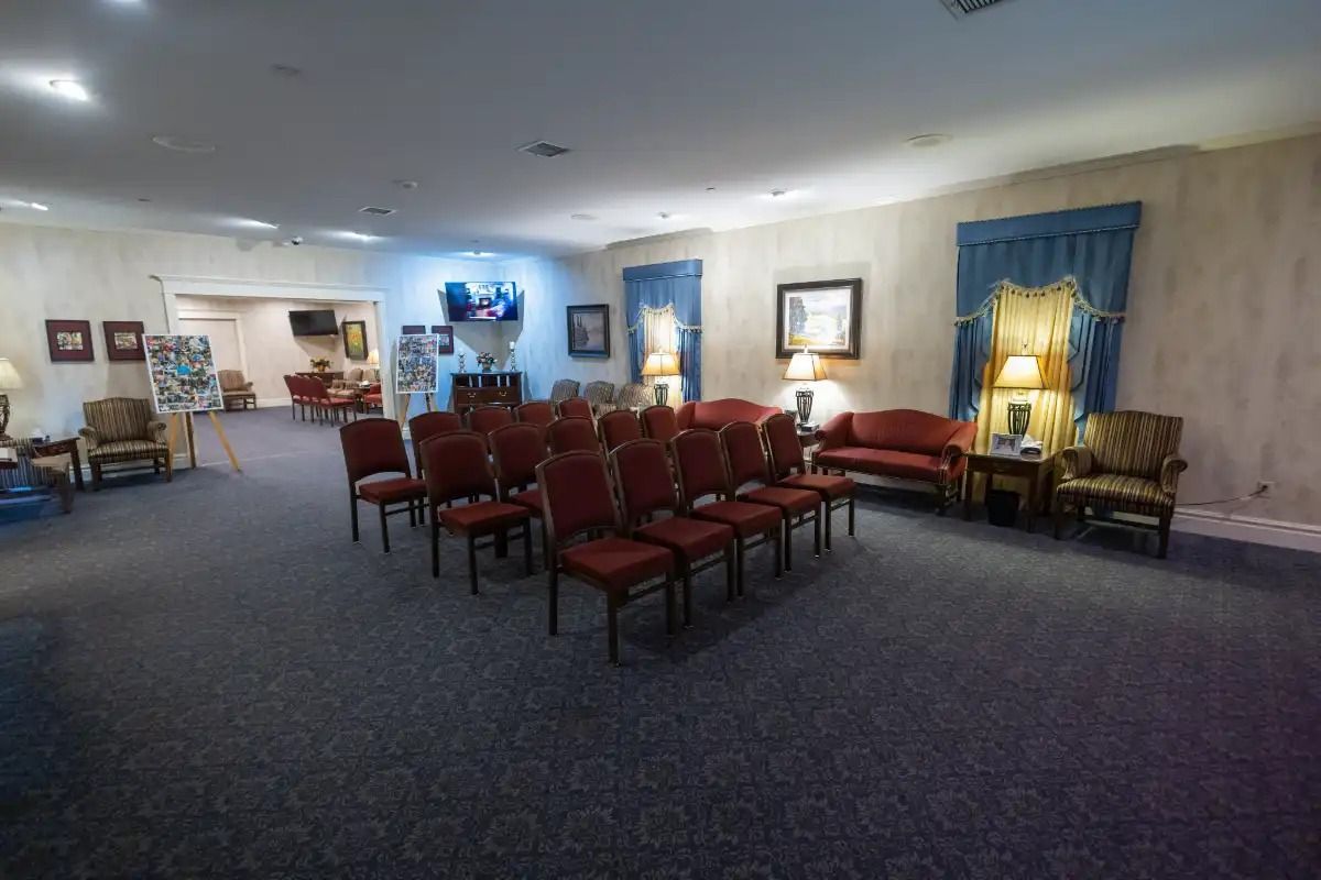 Funeral home with rows of red chairs, seating, a couch, and a television.