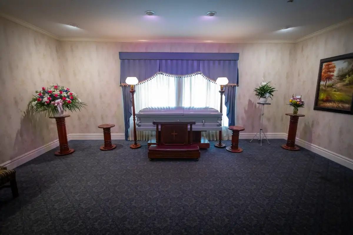 Funeral home interior with casket, floral arrangements, and seating.