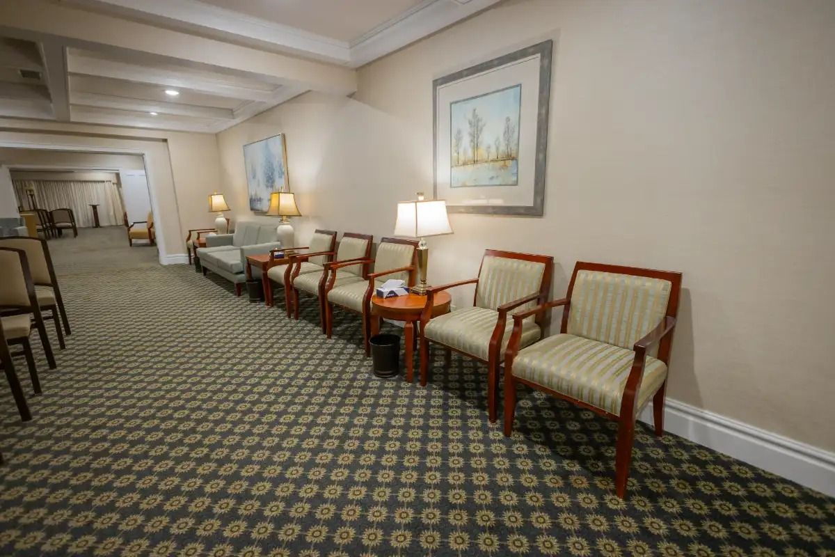 Long hallway with waiting chairs, neutral walls, carpet and artwork.