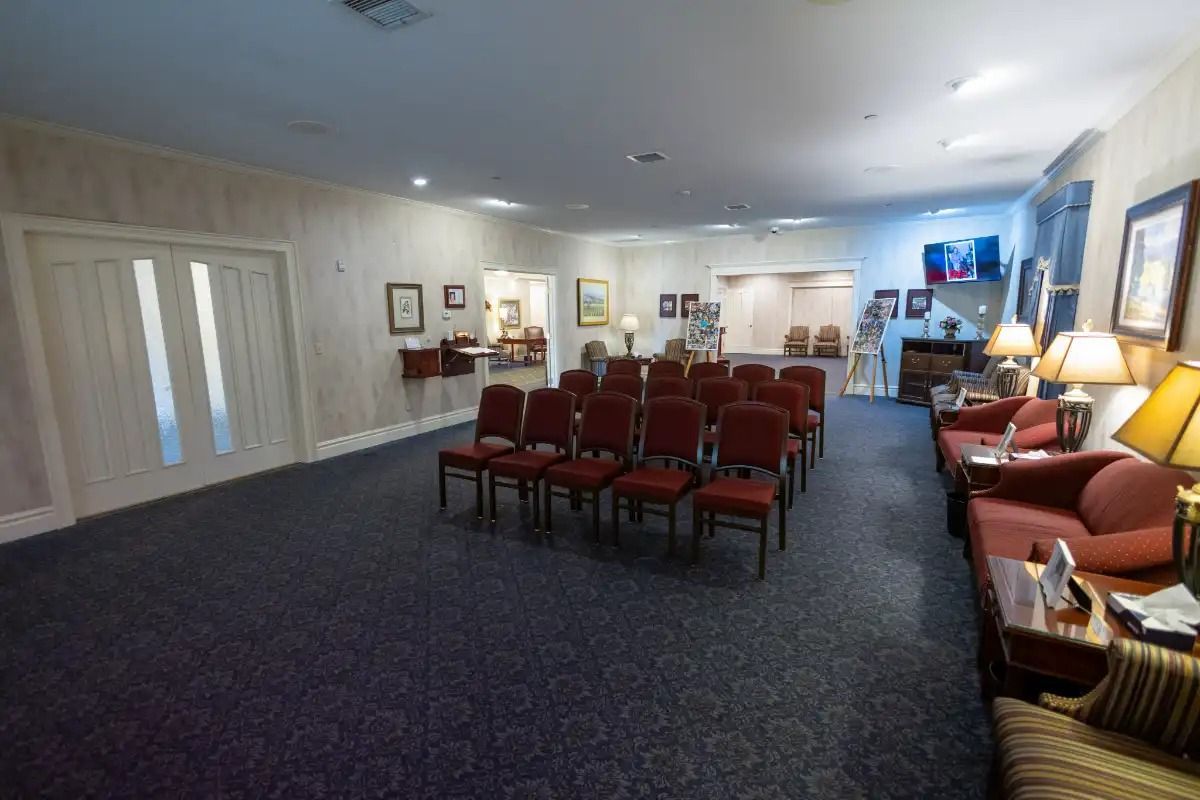 A funeral home interior with red chairs arranged, couches, lamps, and artwork.