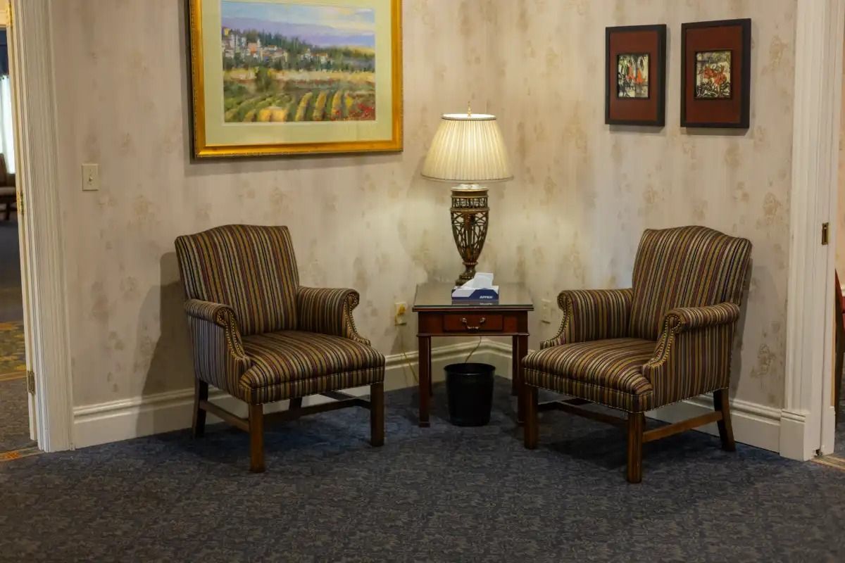 Two striped armchairs with a lamp and small table between them, under artwork.