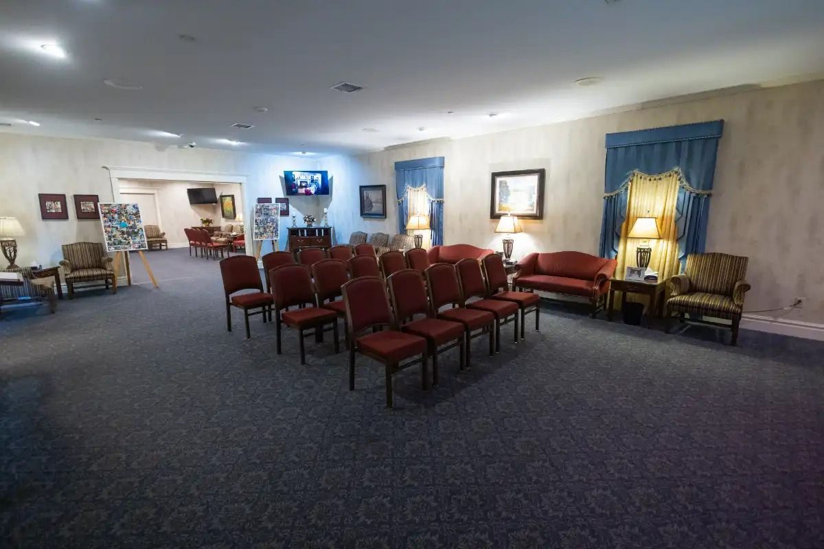 A funeral home viewing room with red chairs arranged for a service.