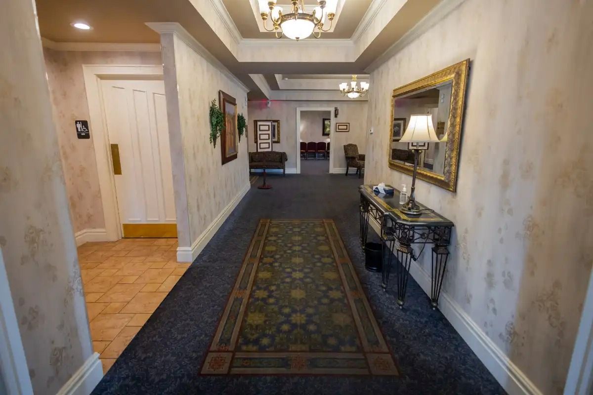 Long hallway with patterned wallpaper, carpet, ornate mirror, and a table.
