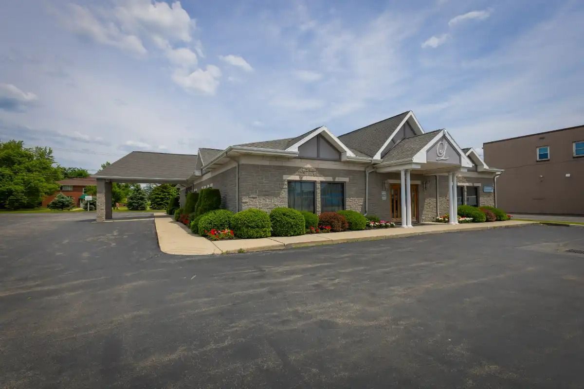 Gray brick building with a dark asphalt parking lot under a cloudy blue sky.